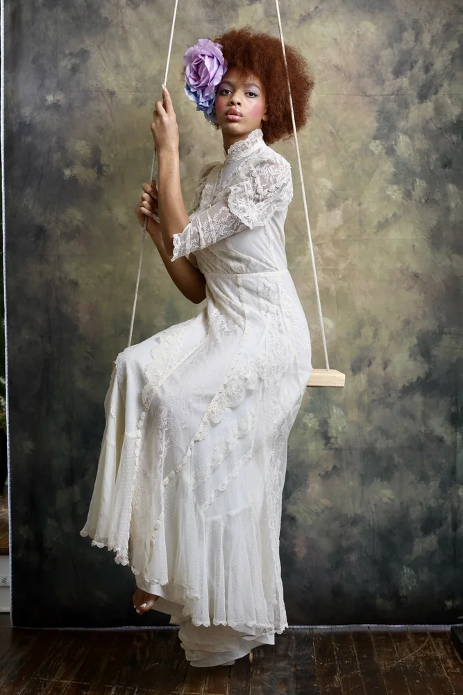 Model in white lace dress seated on a swing, studio editorial
