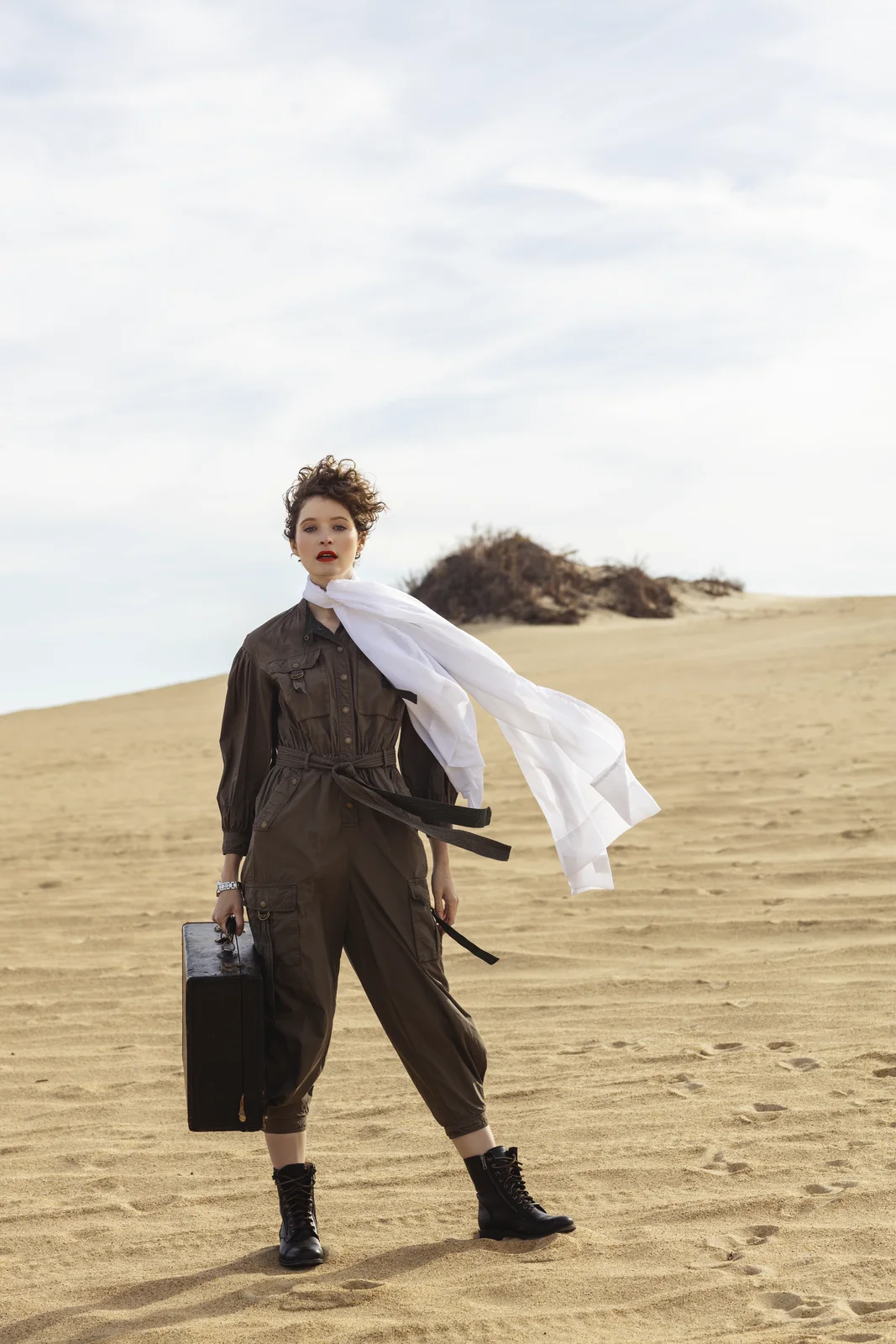 Editorial fashion session on sand dunes — model with vintage suitcase and flowing white scarf